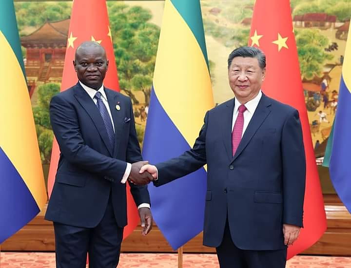 Les Présidents Brice Clotaire Oligui Nguema et Xi Jinping se saluant devant les drapeaux du Gabon et de la Chine